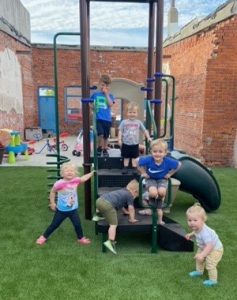 Children playing in updated play space. Playground upgrade artificial turf surfacing installation playground equipment