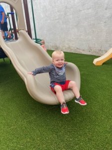 Small boy playing on new slide. Playground company playground installation artificial turf surfacing fall protection